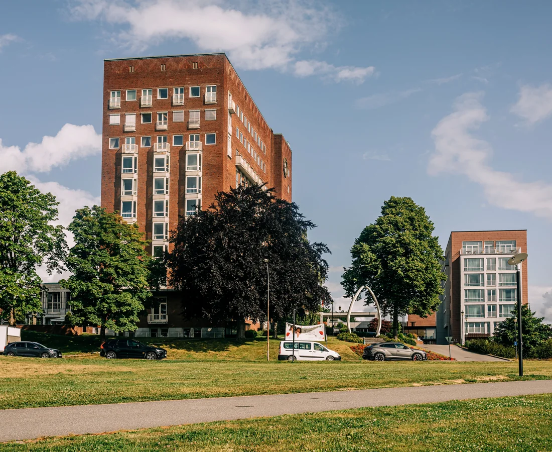 Mehrgeschossige Wohngebäude hinter Bäumen, Rasen und einem Parkweg