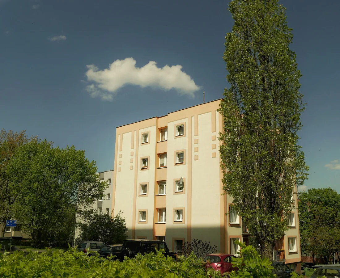Helles Wohngebäude hinter Hecken, Laubbäumen und einer hohen Pappel